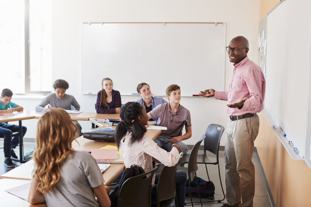 Teacher standing in front of a whiteboard, teaching a classroom of students